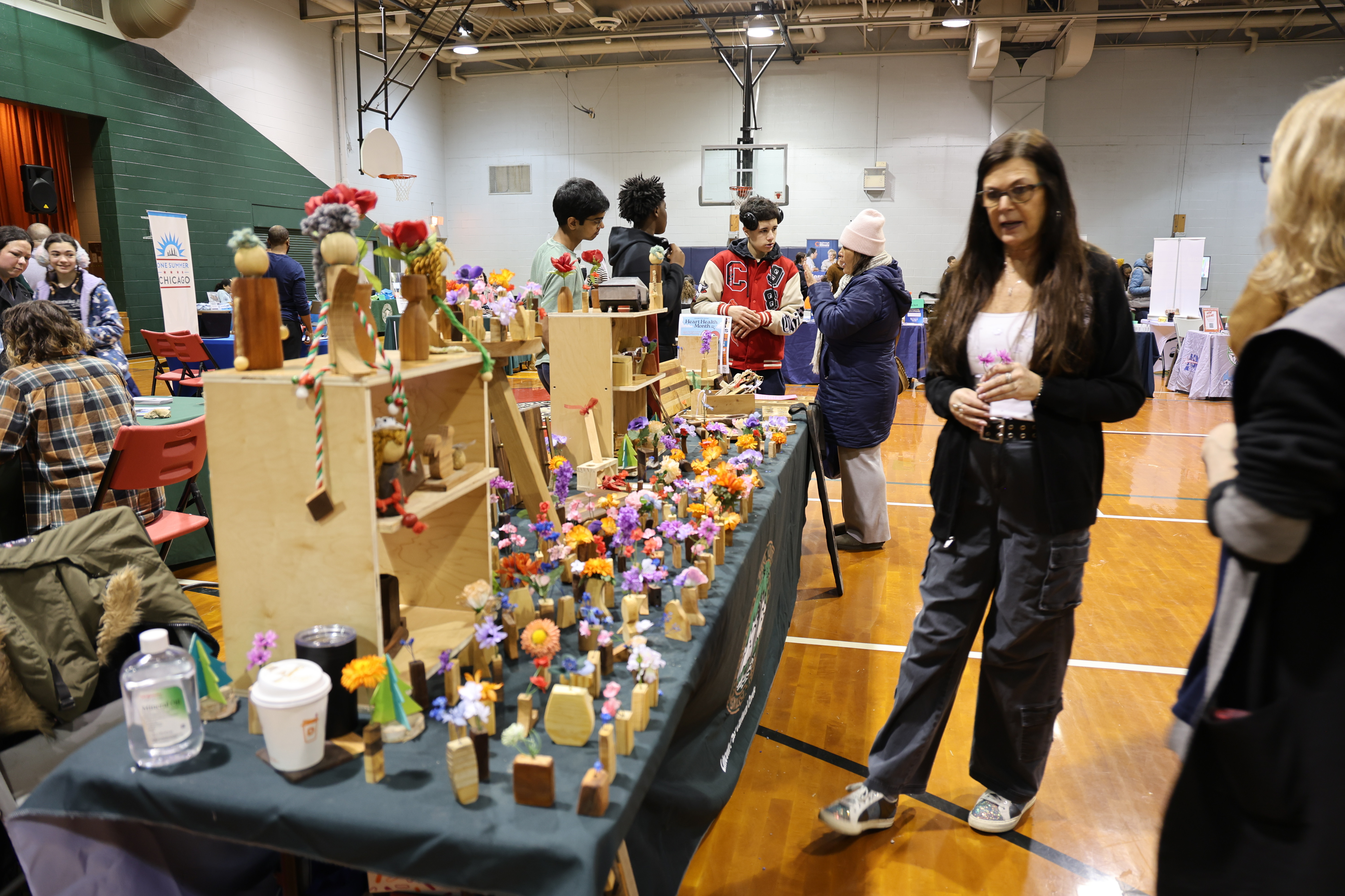 People browse tables of colorful wooden crafts in a busy gym transformed into an indoor market.